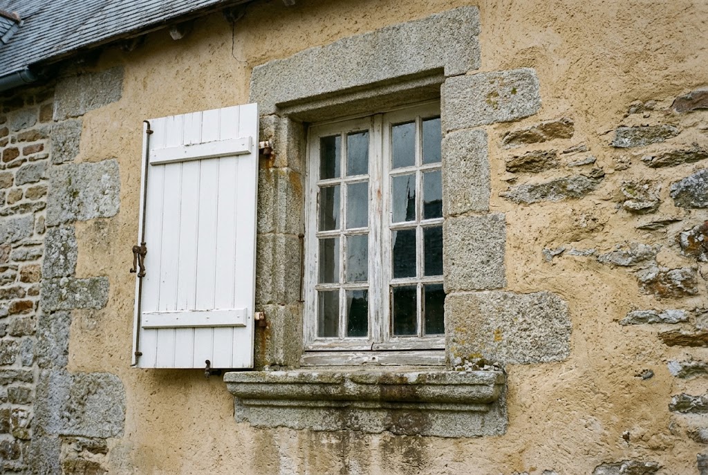 Fenêtre à petits bois en bois peint dans un encadrement de pierre de taille sur une façade ancienne enduite à la chaux